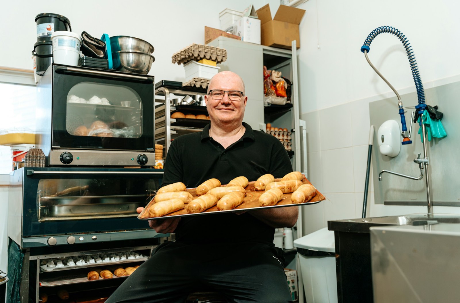 Bakker in de eigen bakkerij met een bakplaat vol broodjes